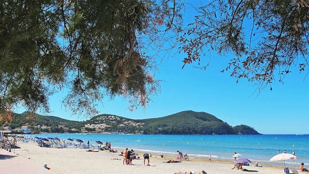 A beach with people sunbathing and swimming, a clear blue sky, and hills in the background.