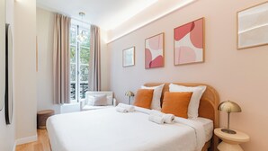 A hotel room with a large bed, a window with curtains, and artwork on the walls.