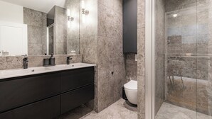 A modern bathroom with a large mirror, dual sinks, a toilet, and a shower area.