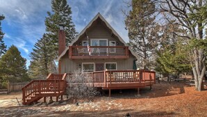 A two-story cabin with a balcony, surrounded by trees.
