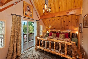 A rustic bedroom with a wooden bed frame, a large window with curtains, and a ceiling with wooden beams.
