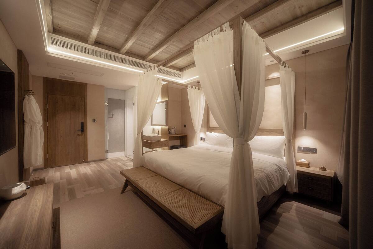 Ein modernes Schlafzimmer mit einem großen Bett, einer Bank, einem Nachttisch, einem Spiegel und einem Duschbereich.