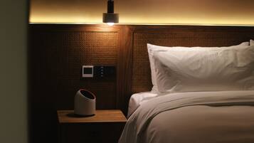 Una habitación de hotel con una cama, una mesita de noche con lámpara y un termostato.