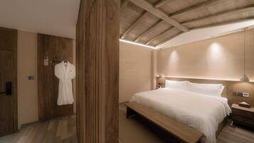 A bedroom with a wooden ceiling, a large bed with white linens, a wooden bench, and a robe hanging on a hook.