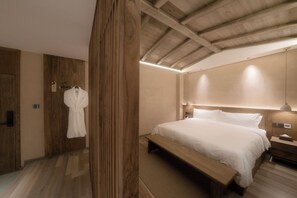 A bedroom with a wooden ceiling, a large bed with white linens, a wooden bench, and a robe hanging on a hook.