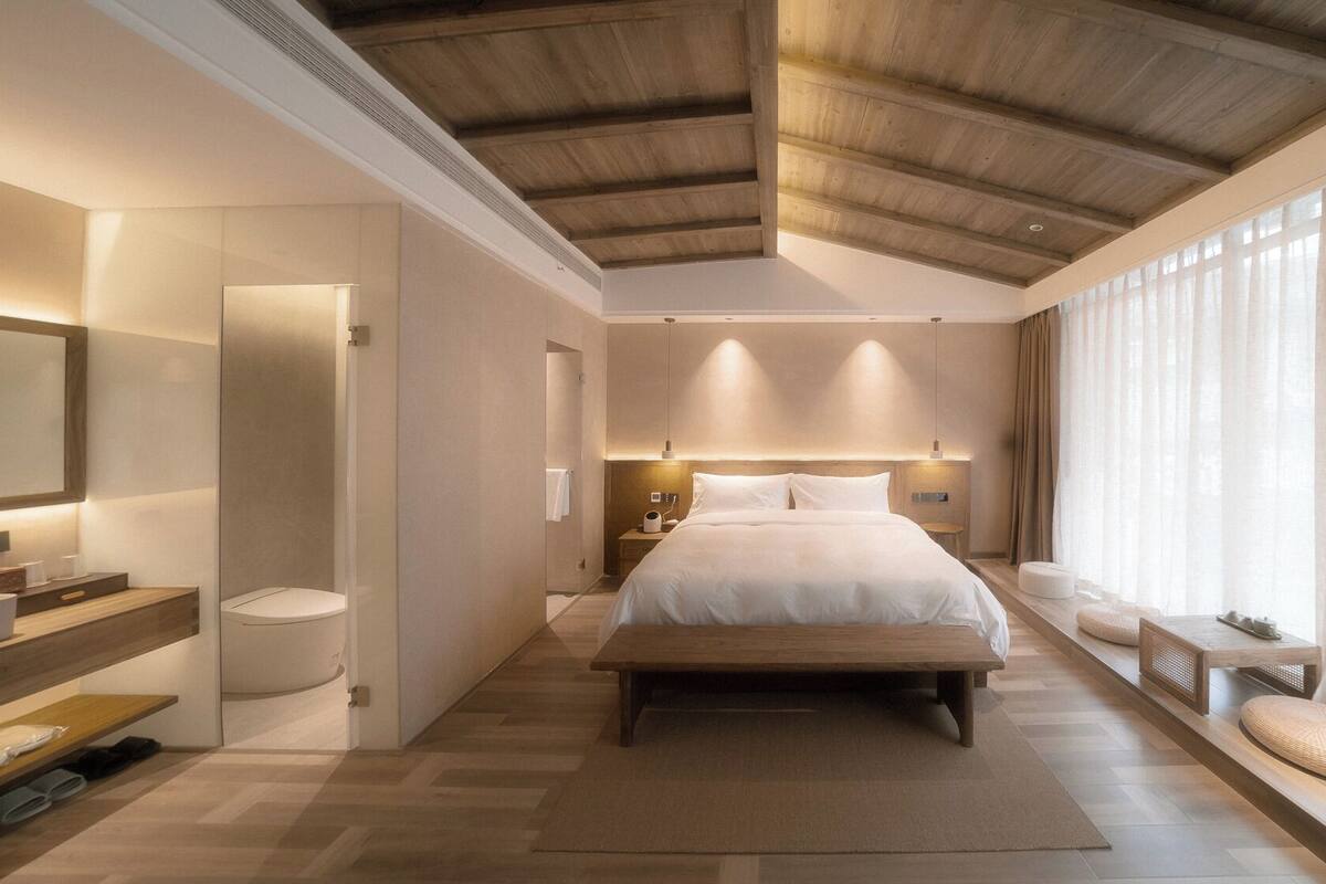 Ein modernes Schlafzimmer mit einem großen Bett, einem Nachttisch, einem Spiegel und einem Fenster mit durchsichtigen Vorhängen.