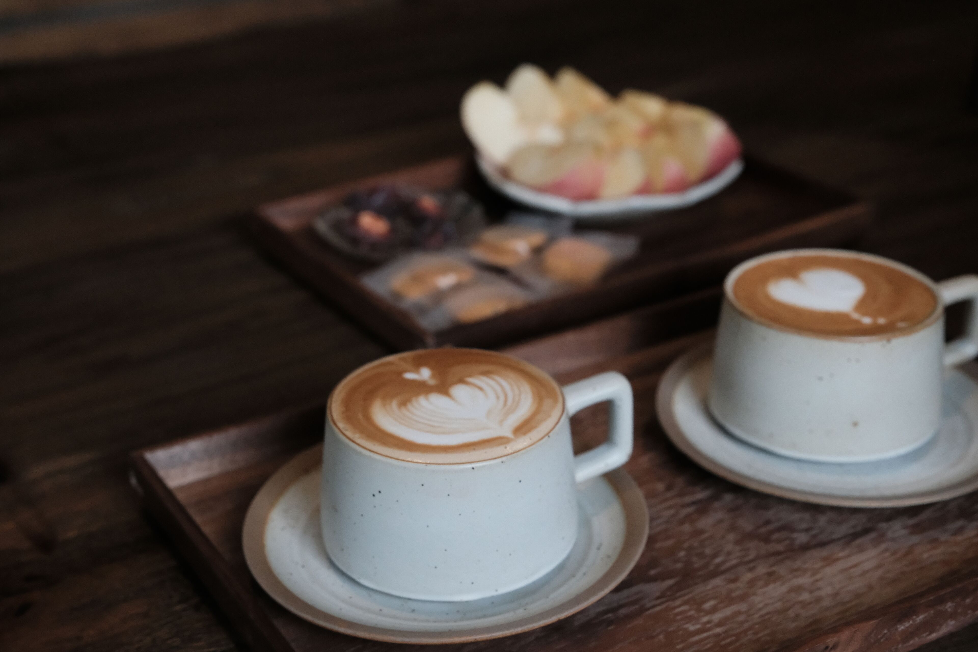 To hvide kaffekopper med hjerteformet latte-kunst på en træbakke.