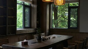 A dining area with a large wooden table, chairs, and a window with a view of greenery. - Shishe Spring Designer Homestay (Chengdu)