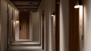 A long, narrow hallway with a wooden door at the end, light fixtures on the walls, and a ceiling with a textured pattern. - Shishe Spring Designer Homestay (Chengdu)