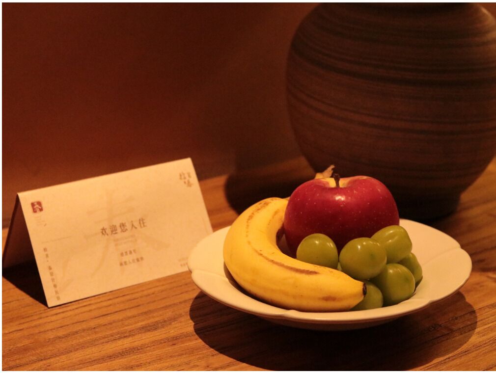Prato com uma maçã, banana e uvas sobre uma mesa de madeira, ao lado de um cartão com caracteres chineses.