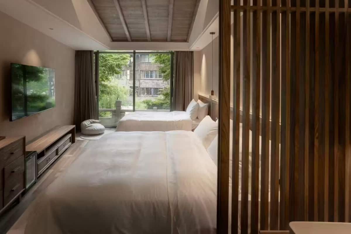 Ein modernes Schlafzimmer mit einem großen Bett, einem an der Wand befestigten Fernseher und Blick ins Grüne.