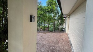 A covered outdoor area with a security camera, gravel ground, and surrounding greenery. - Beautiful 4 BDR House with ensuite and A/C (Redbank Plains)
