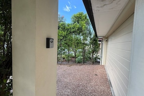A covered outdoor area with a security camera, gravel ground, and surrounding greenery.