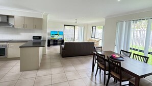 A modern kitchen with a dining area, a sofa, and a TV. - Beautiful 4 BDR House with ensuite and A/C (Redbank Plains)