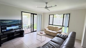 A living room with a TV, a sofa, a coffee table, and a ceiling fan. - Beautiful 4 BDR House with ensuite and A/C (Redbank Plains)