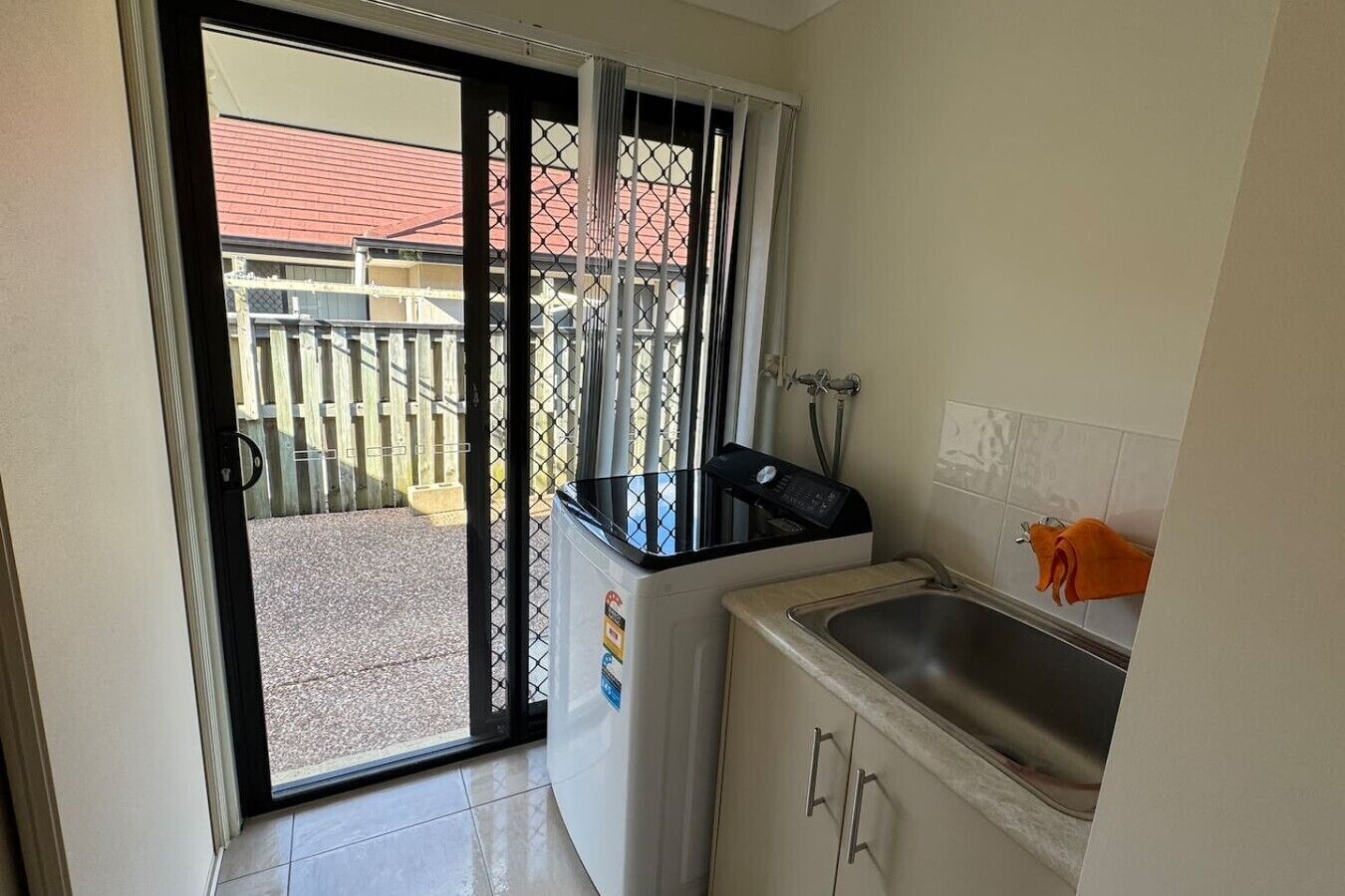Una cocina con un lavamanos, un refrigerador y una ventana con vistas a un edificio y una valla.