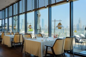 A restaurant with tables set for dining, large windows offering a city view, and hanging pendant lights. - UrCove by Hyatt Nanjing Confucius Temple (Nanjing)