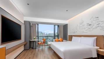 A modern hotel room with a large bed, a desk, a chair, a TV, and a city view.