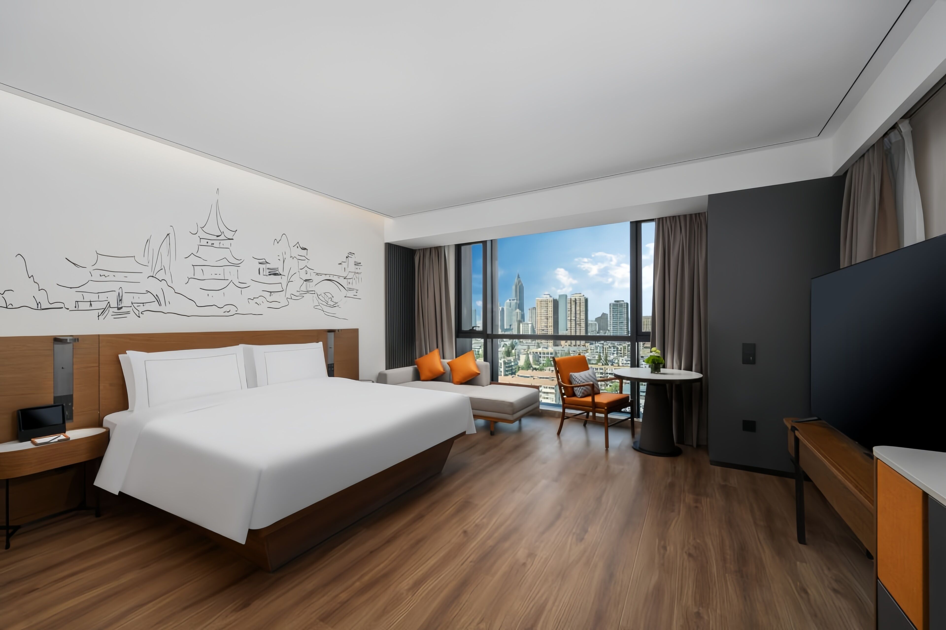 A hotel room with a large bed, a desk, a chair, a TV, and a view of a cityscape.