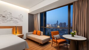 A hotel room with a bed, sofa, chair, table, and a large window with a city view. - UrCove by Hyatt Nanjing Confucius Temple (Nanjing)
