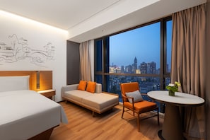 Une chambre d’hôtel équipée d’un lit, d’un canapé, d’une chaise, d’une table et d’une grande fenêtre donnant sur la ville.