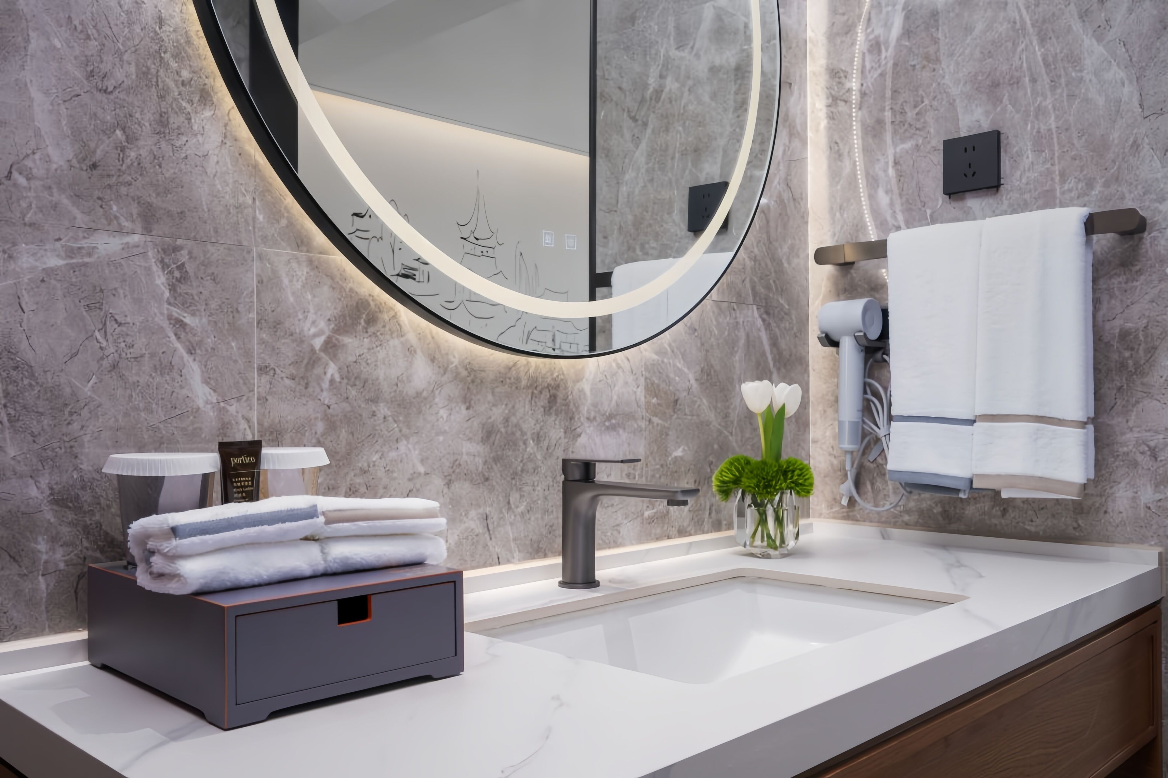 Un baño moderno con pared de mármol, un espejo redondo, un lavabo y un perchero para toallas.