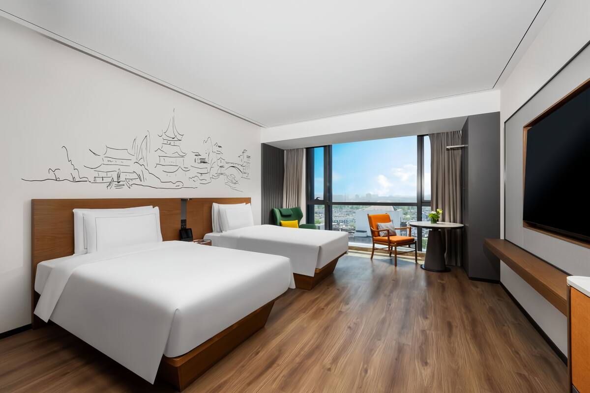 A hotel room with two beds, a TV, a balcony with a view, and a wall art piece.