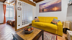 A yellow sofa with pillows, a wooden coffee table with a fruit bowl, a painting of a sunset, and a traditional Japanese shoji screen.