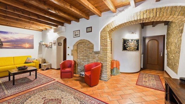 A living room with a yellow sofa, two red chairs, a wooden coffee table, and a fireplace with a stone arch.