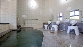 A public restroom with a tiled floor, a large mirror, and a shower area.