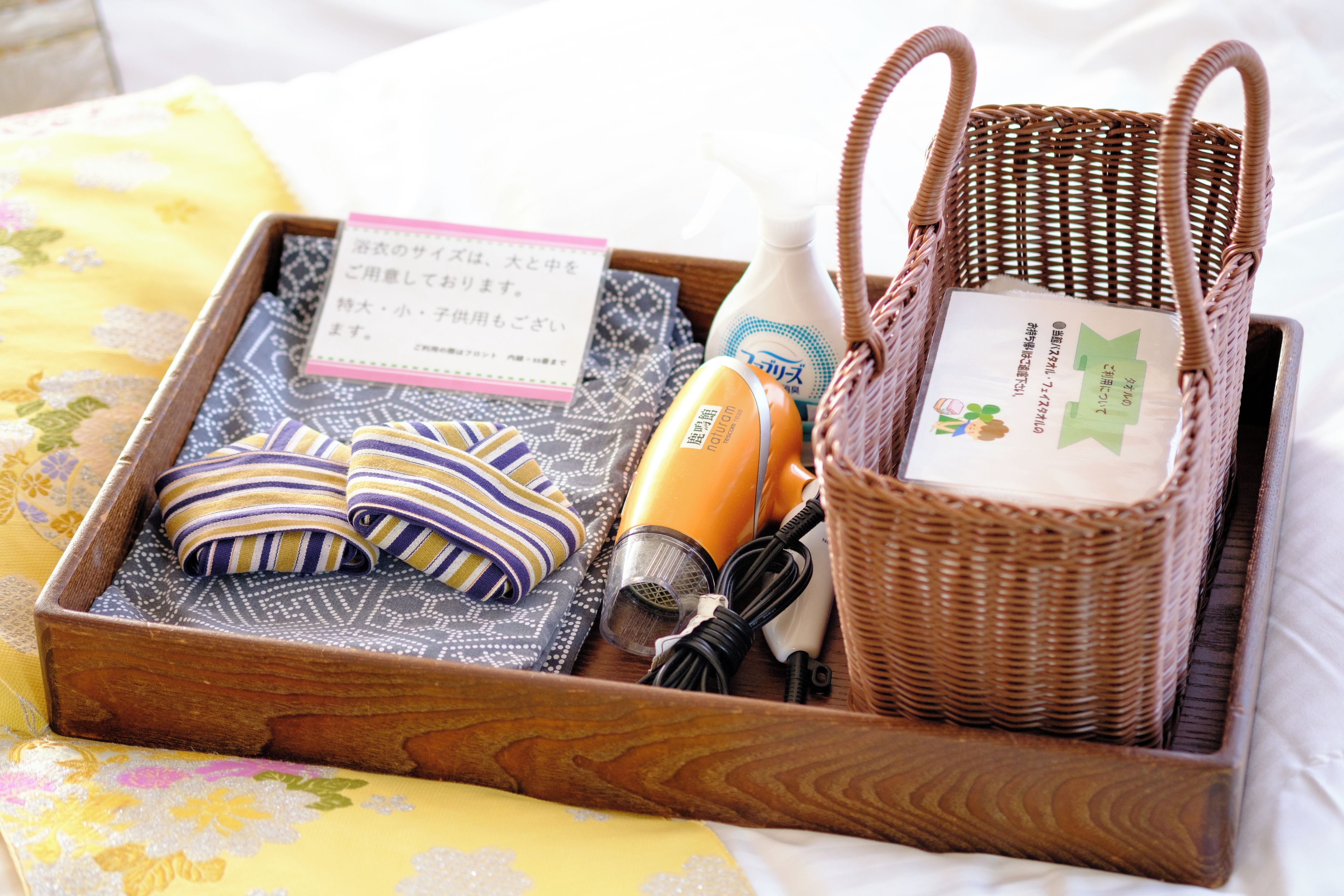 A wooden tray with a woven basket, a hairdryer, a bottle of lotion, and a folded towel.
