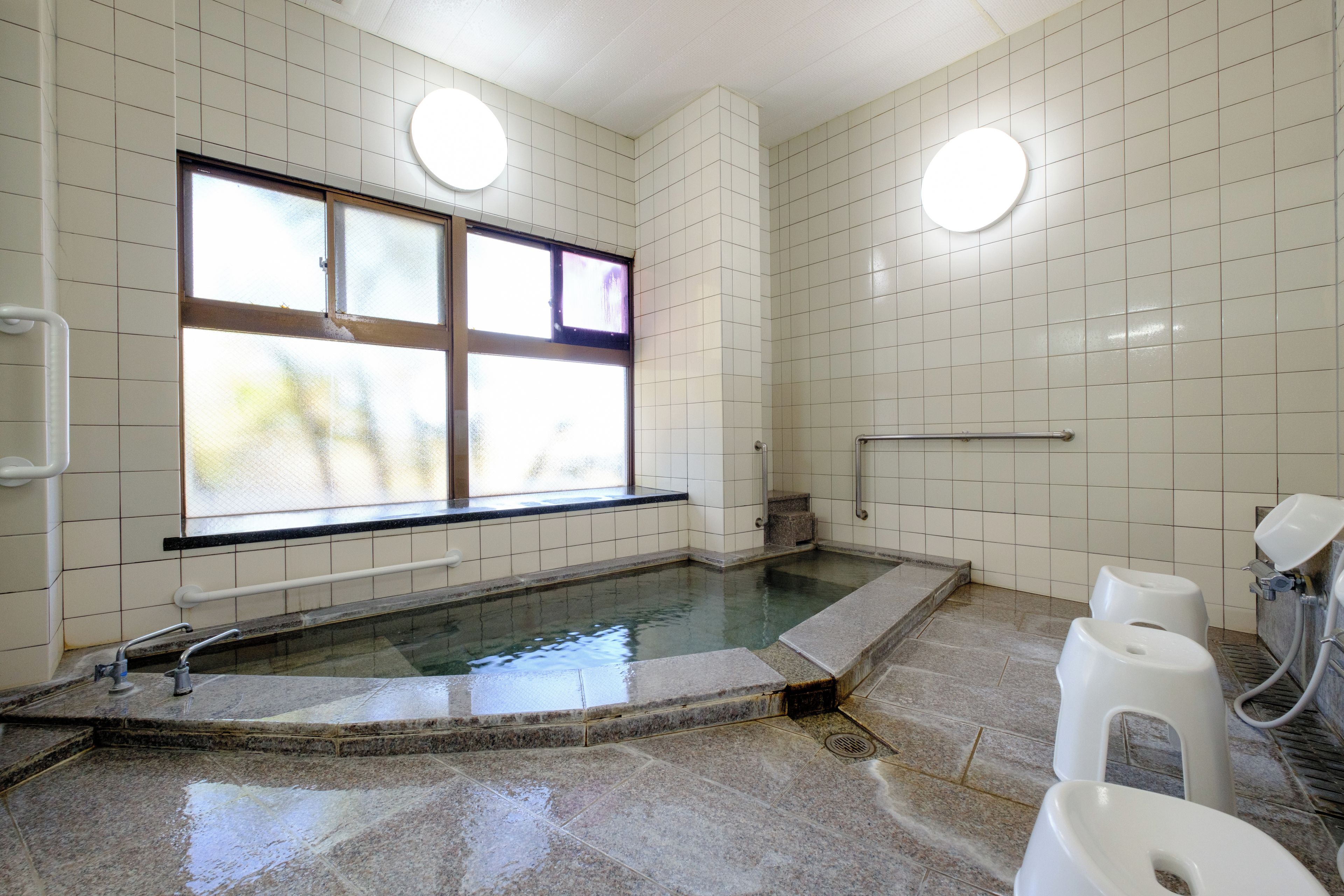 A public restroom with a large window, a tiled wall, a granite floor, and a urinal.