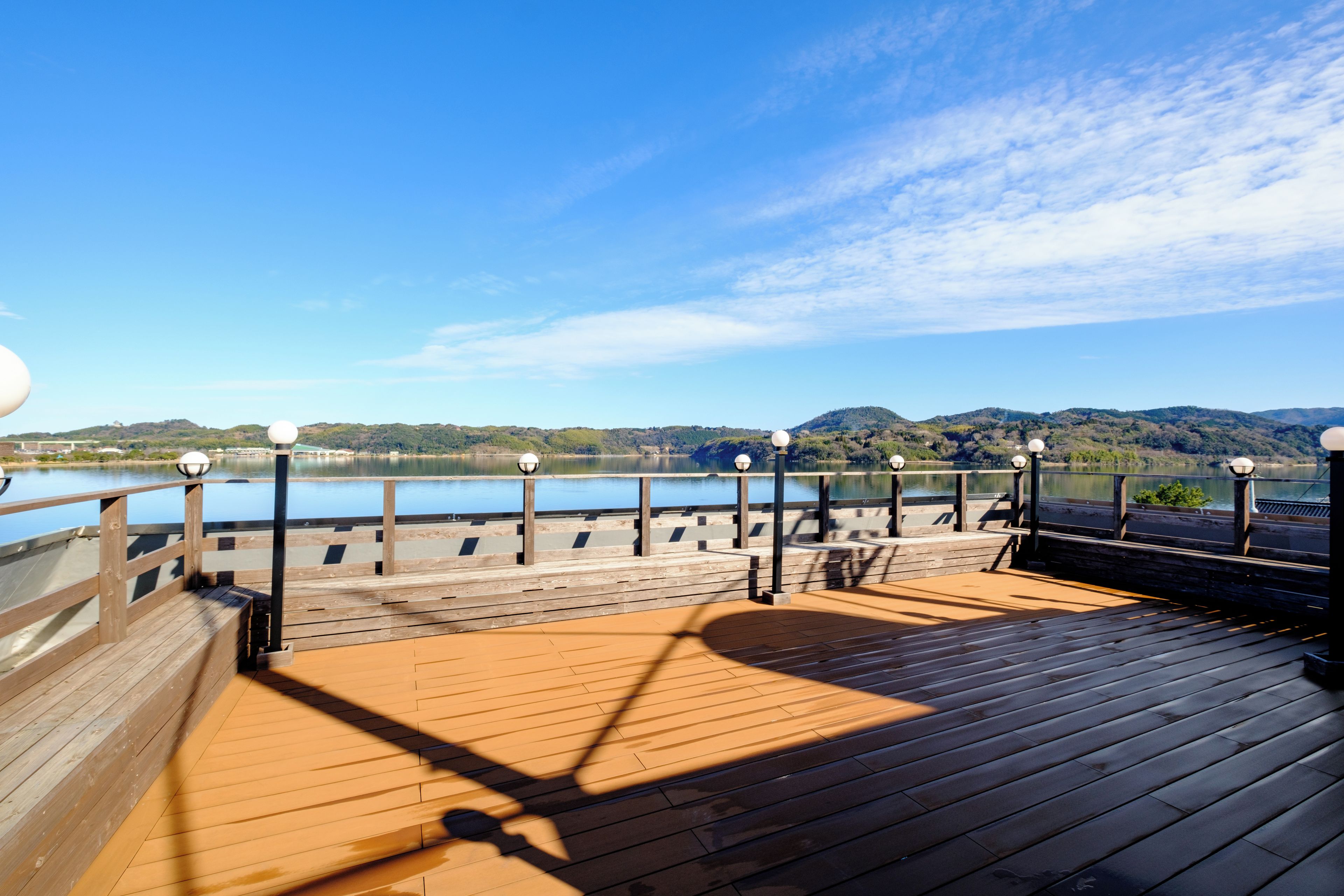 A wooden deck with a railing overlooking a body of water and hills.