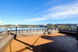 A wooden deck with a railing overlooking a body of water and hills. - Rokumeikan (Yurihama)