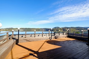 Una terraza de madera con barandilla, con vista a un cuerpo de agua y colinas.