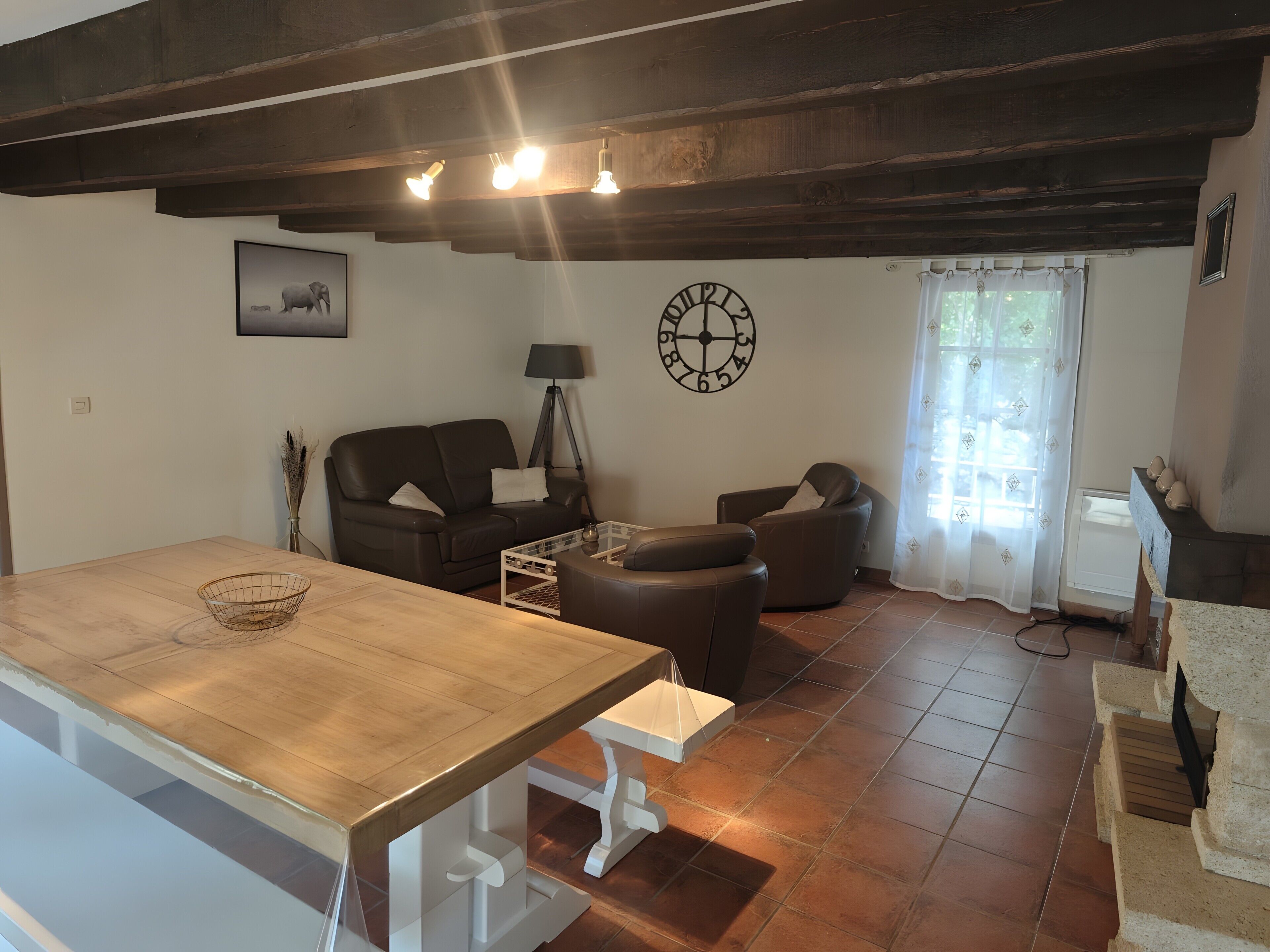 Een woonkamer met een houten tafel, twee banken, een lamp, een klok en een raam met gordijnen.