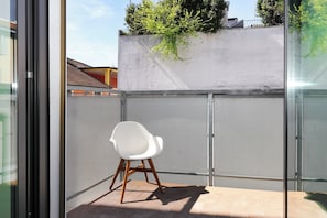 A balcony with a white chair, a metal fence, and a view of buildings and trees. - Delightful Family Flat with Terrace (Milan)
