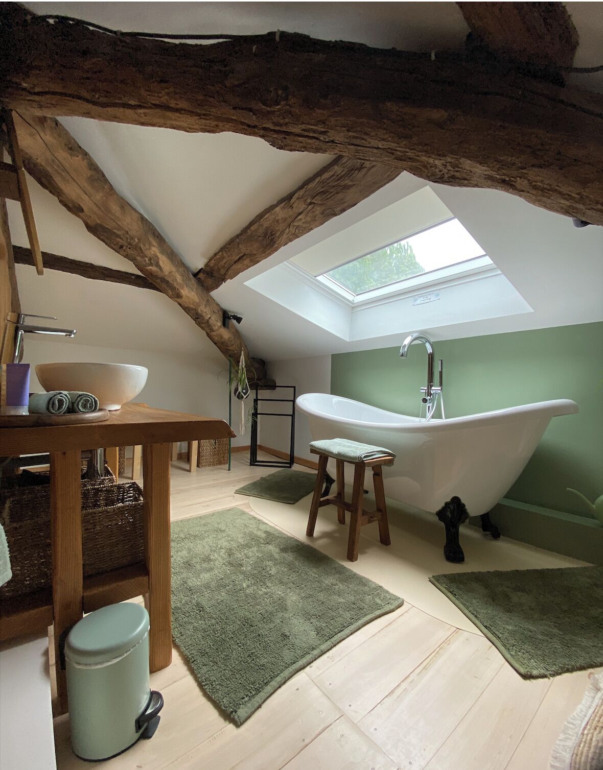 A rustic bathroom with a skylight, a freestanding bathtub, a wooden vanity, and a green rug.