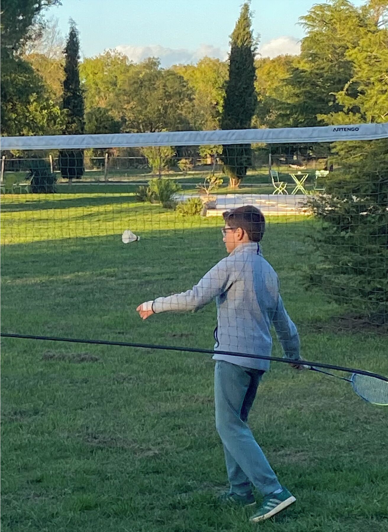 Une personne jouant au tennis sur un court en gazon, avec un filet en arrière-plan.