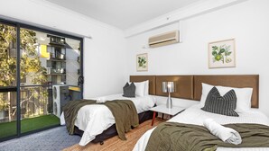 Une chambre d’hôtel moderne avec deux lits, un balcon et une vue sur un immeuble doté de balcons.