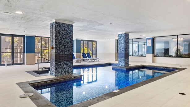 Une piscine intérieure aux murs carrelés, un espace détente avec des fauteuils et de grandes fenêtres.