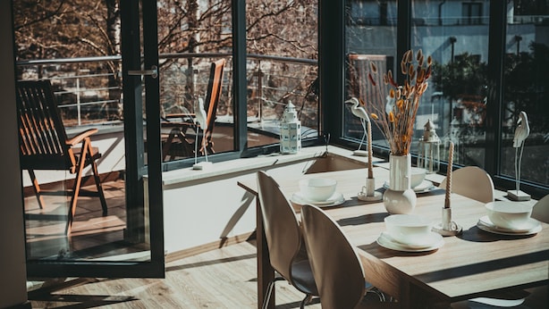 A modern dining area with a wooden table set for four, large windows offering a view of trees and buildings. - Violino 6 Os b Nowoczesny 5 min do Pla y (Trzebiatow)