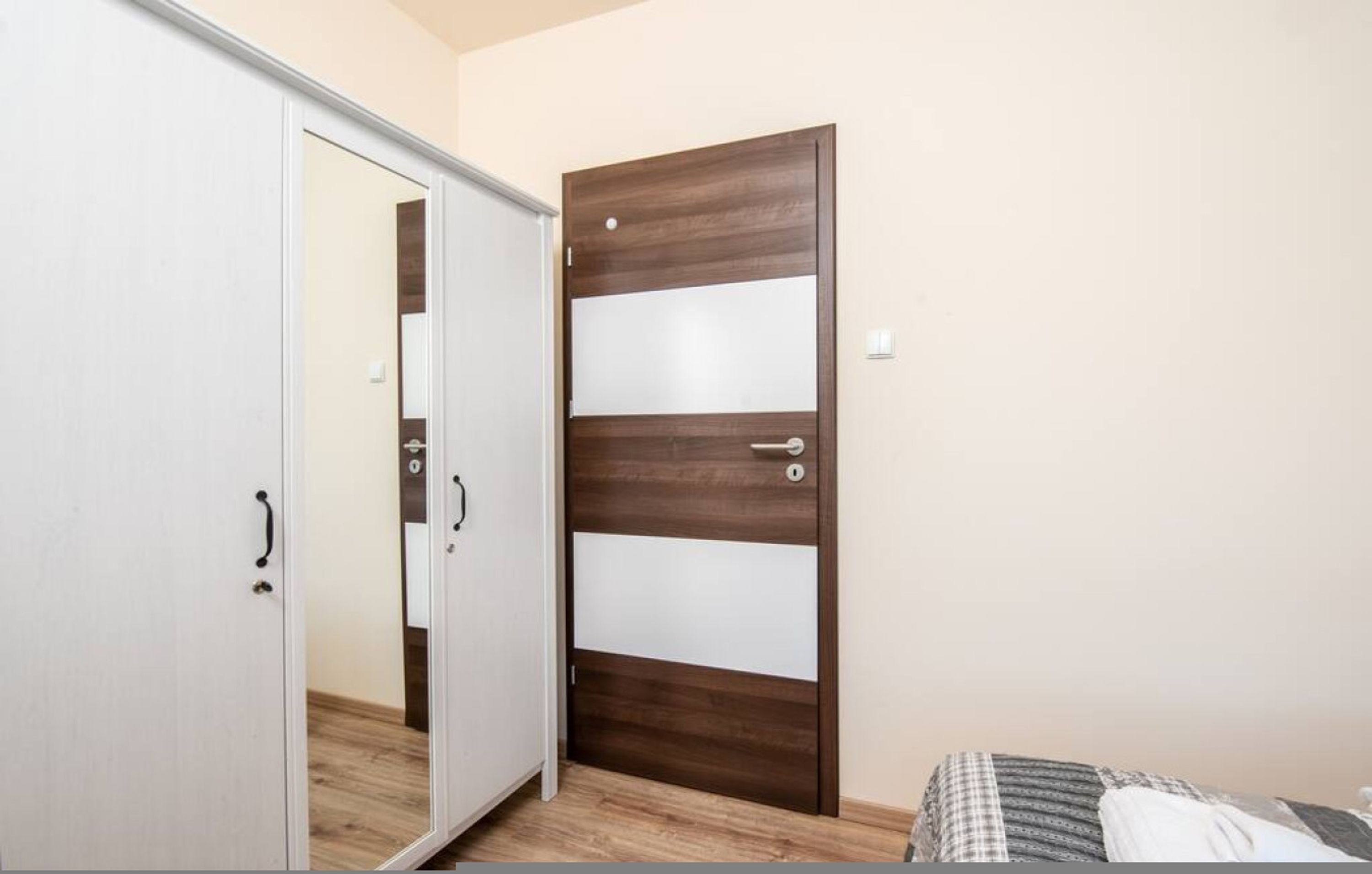 A bedroom with a wardrobe, a bed with a patterned bedspread, and a wooden door with frosted panels.