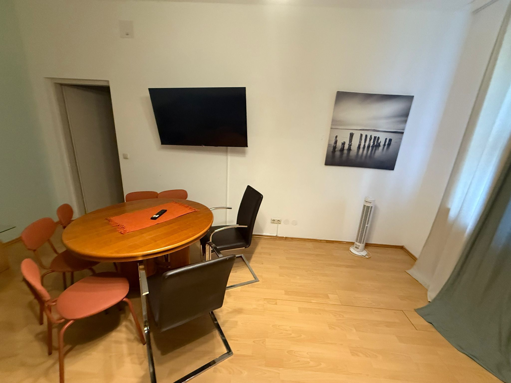 Une salle de conférence avec une table ronde, six chaises, un téléviseur et un tableau accroché au mur.