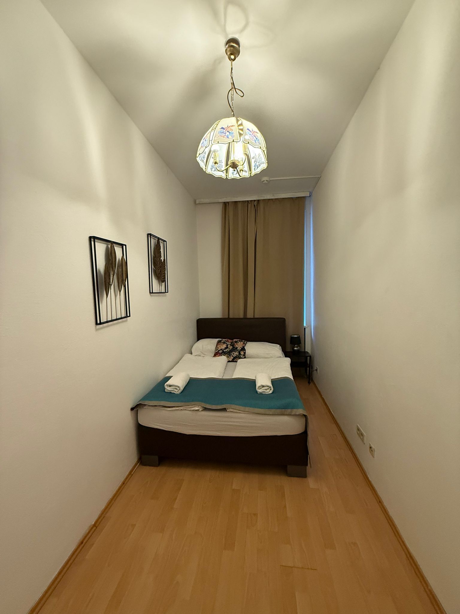 A bedroom with a bed, a chandelier, a nightstand, and two wall-mounted pictures.