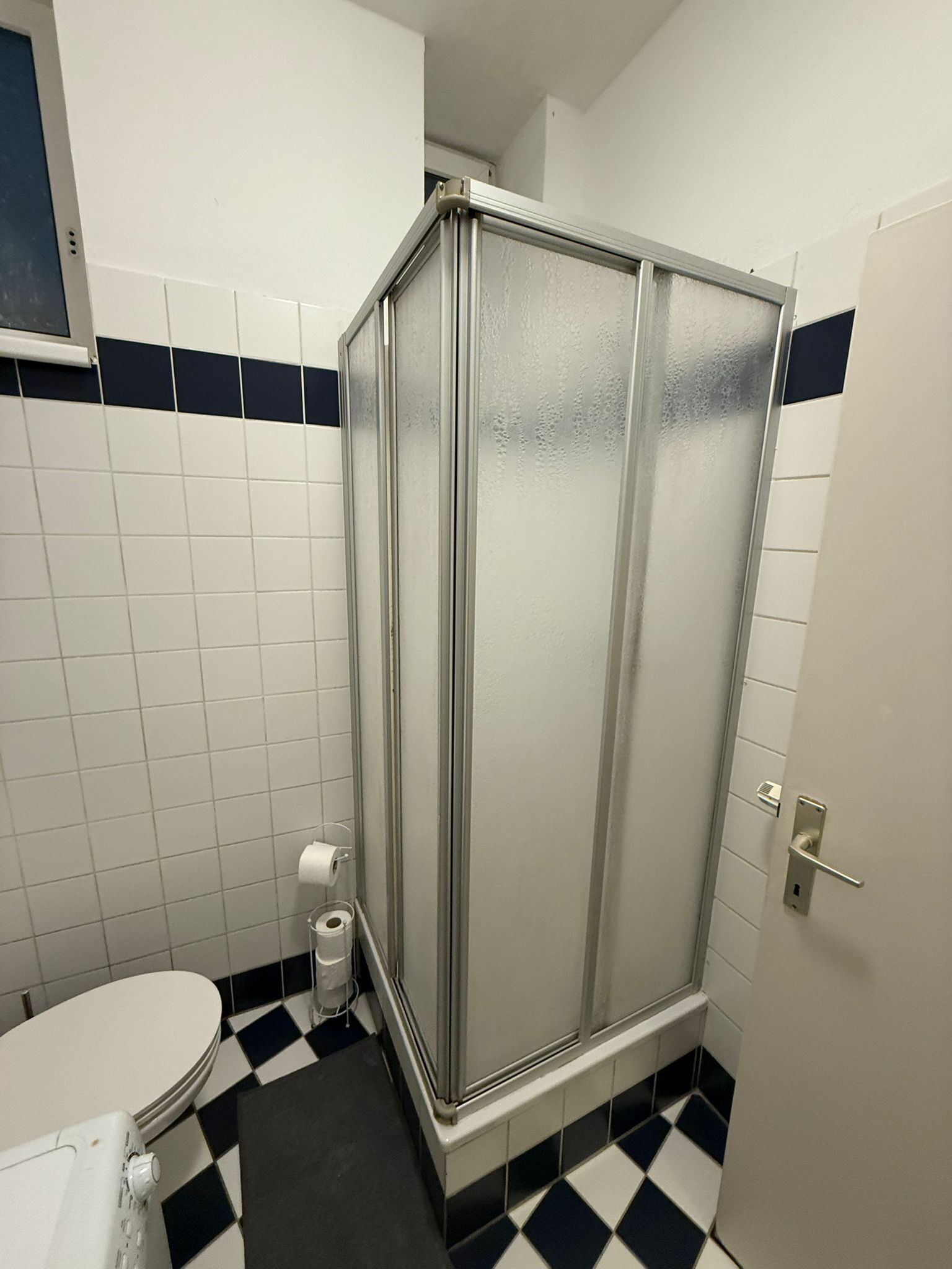 Un bagno con un water bianco, una doccia vetrata e un pavimento a scacchi.
