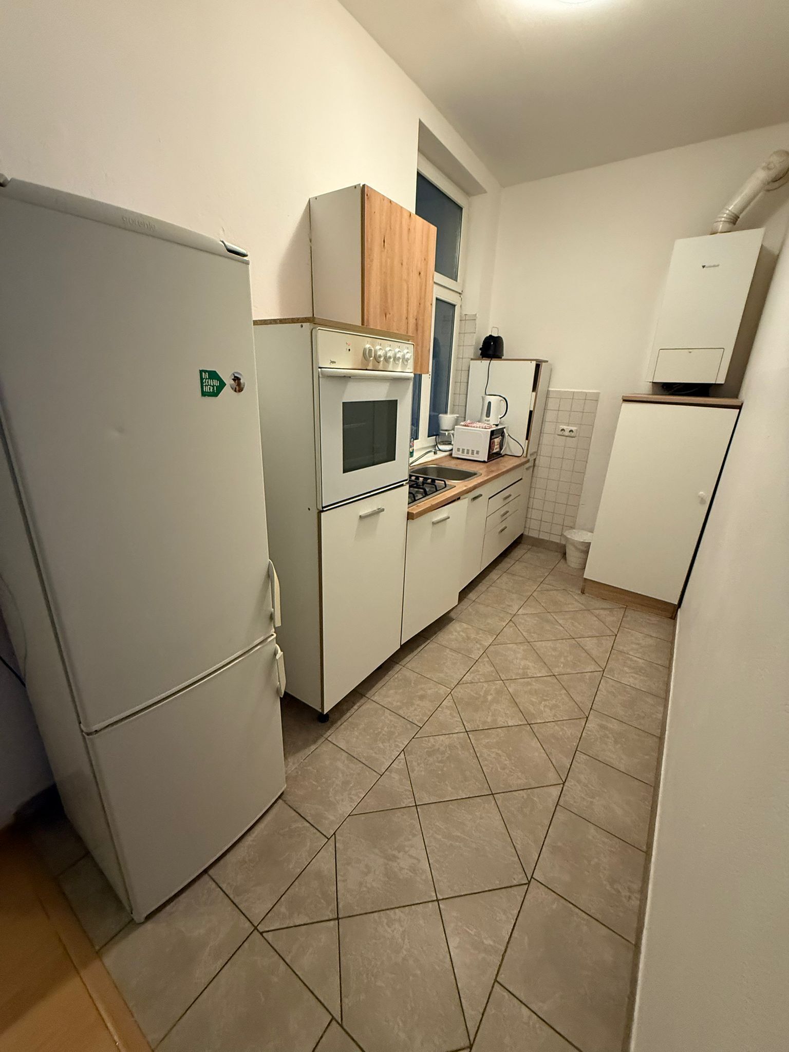 A compact kitchen with white cabinets, a built-in oven, a refrigerator, and a wooden countertop.
