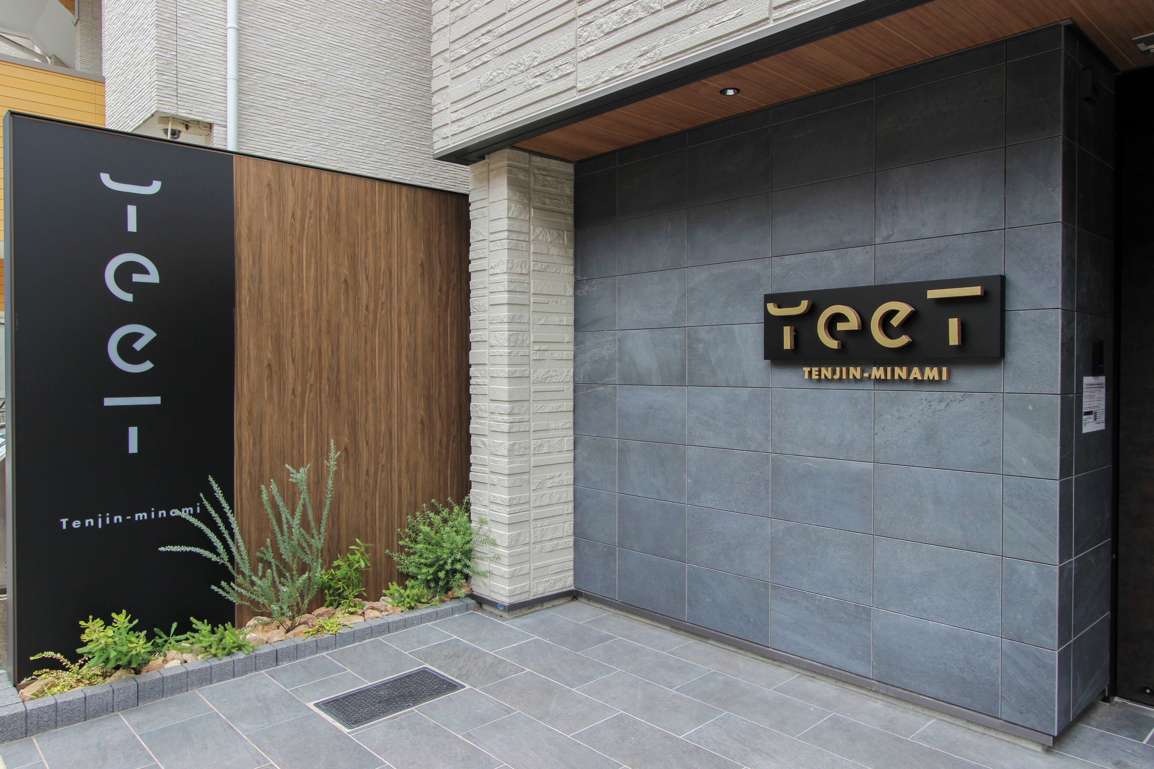 A building entrance with a black sign reading 'J-ice TENJIN-MINAMI' and a grey tiled wall with a sign 'TEC'T TENJIN-MINAMI'.