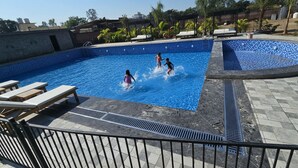 A swimming pool with three children playing, surrounded by lounge chairs and a tiled deck. - Evergreen Resort And SPA  The Lychee  (Kaladhungi)
