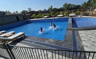 Piscina com três crianças brincando, cercada por cadeiras de espreguiçadeira e um deck revestido.